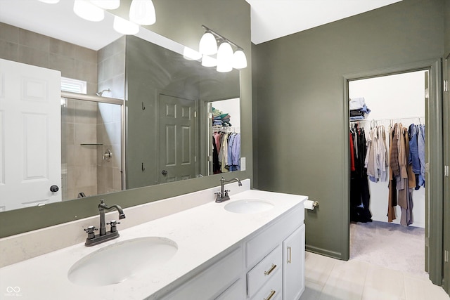 full bathroom featuring a tile shower, double vanity, a sink, and a walk in closet