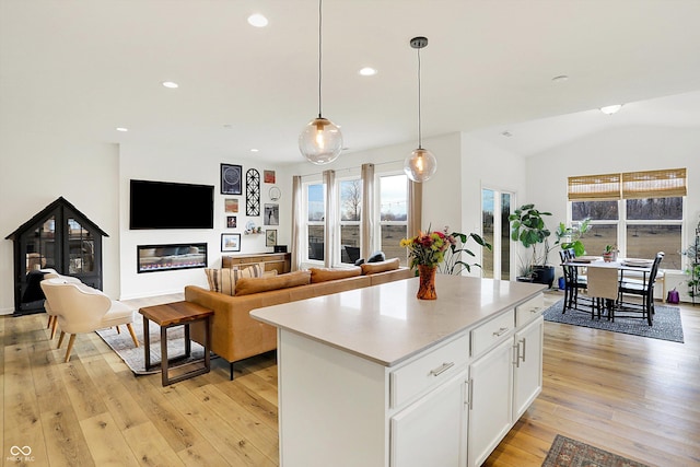 kitchen featuring white cabinets, a glass covered fireplace, a kitchen island, light wood-type flooring, and pendant lighting