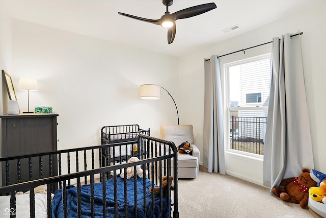 carpeted bedroom with a crib, visible vents, baseboards, and a ceiling fan