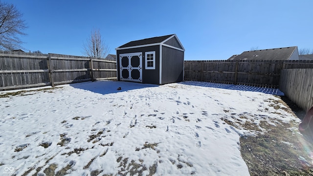 yard covered in snow featuring a fenced backyard, an outdoor structure, and a shed