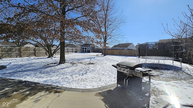 yard layered in snow featuring a trampoline, a fenced backyard, an outdoor structure, and a storage shed