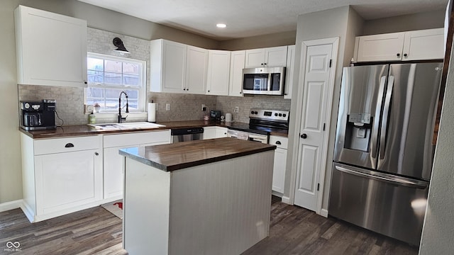 kitchen featuring stainless steel appliances, a sink, white cabinets, a center island, and dark wood-style floors