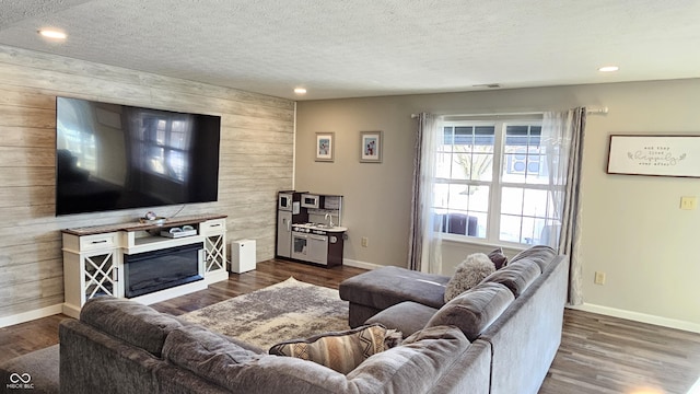 living area featuring dark wood-style floors, a glass covered fireplace, wood walls, and a textured ceiling