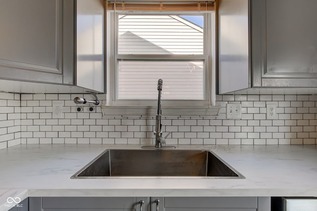 kitchen with light stone countertops, gray cabinets, backsplash, and a sink