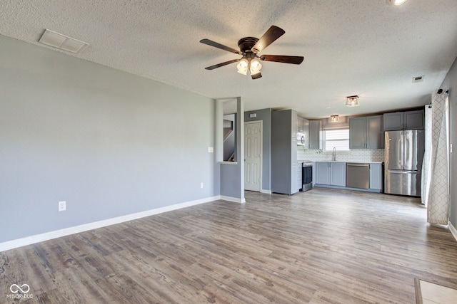 unfurnished living room featuring visible vents, light wood-style flooring, baseboards, and a sink