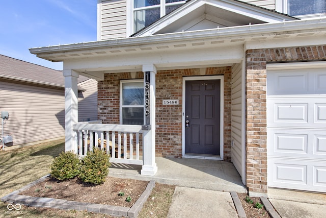 doorway to property featuring an attached garage, brick siding, and covered porch