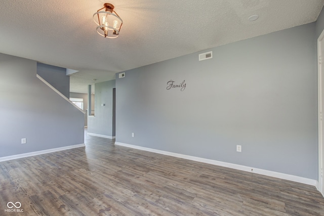 unfurnished room featuring visible vents, baseboards, a textured ceiling, and wood finished floors