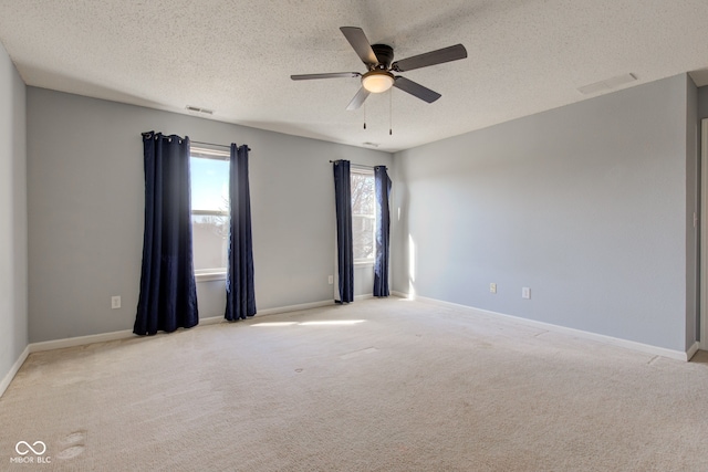 spare room with a textured ceiling, carpet flooring, visible vents, and ceiling fan