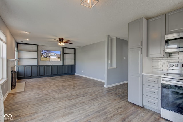 kitchen with stainless steel microwave, light wood-type flooring, decorative backsplash, gray cabinets, and range with electric stovetop