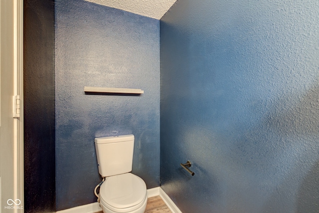 bathroom with a textured wall, toilet, baseboards, and wood finished floors