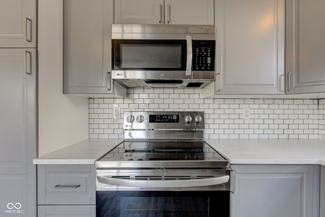 kitchen featuring tasteful backsplash, appliances with stainless steel finishes, gray cabinetry, and light stone countertops