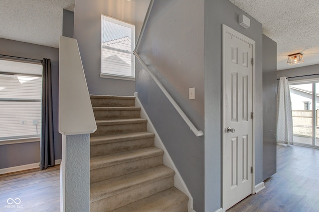 staircase with wood finished floors, baseboards, and a textured ceiling