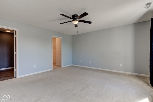 unfurnished bedroom featuring visible vents, baseboards, a spacious closet, a textured ceiling, and light colored carpet