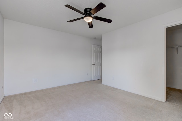 unfurnished bedroom with a spacious closet, a ceiling fan, a closet, and light carpet