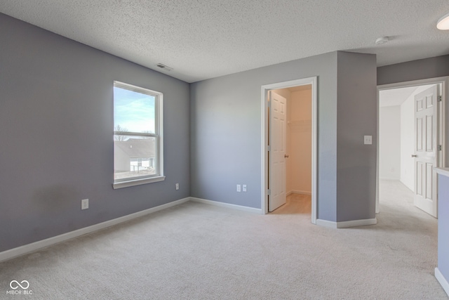 unfurnished bedroom with visible vents, a walk in closet, a textured ceiling, baseboards, and light colored carpet