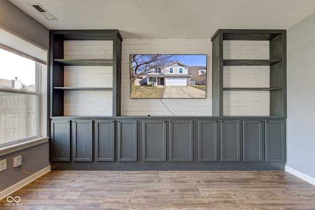 spare room with baseboards, visible vents, light wood finished floors, and a textured ceiling