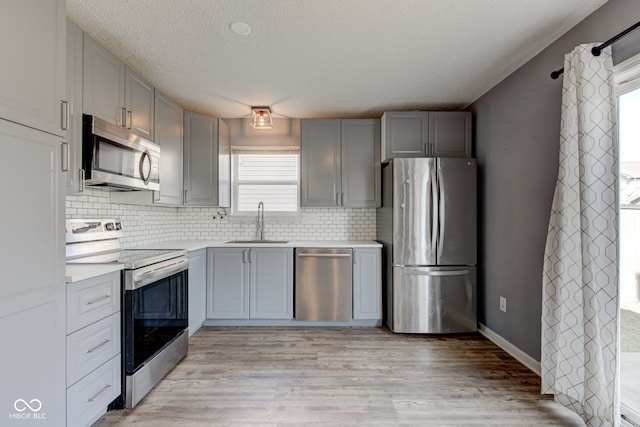 kitchen featuring a sink, gray cabinetry, light countertops, stainless steel appliances, and light wood-style floors