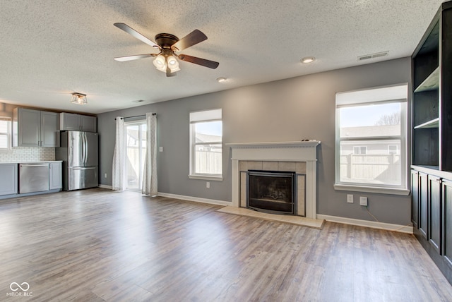 unfurnished living room featuring visible vents, light wood-style flooring, a ceiling fan, baseboards, and a tile fireplace