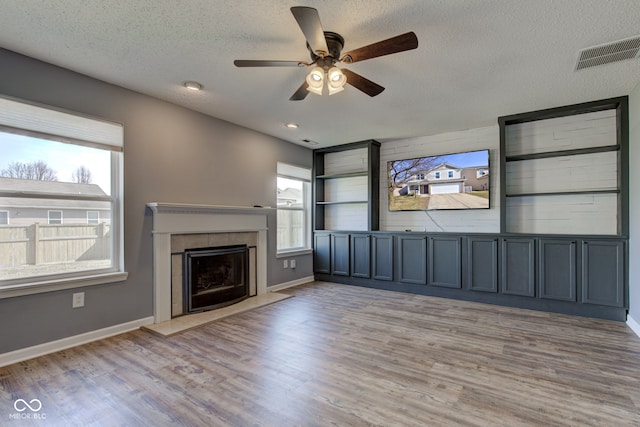 unfurnished living room featuring visible vents, plenty of natural light, a tiled fireplace, and light wood finished floors