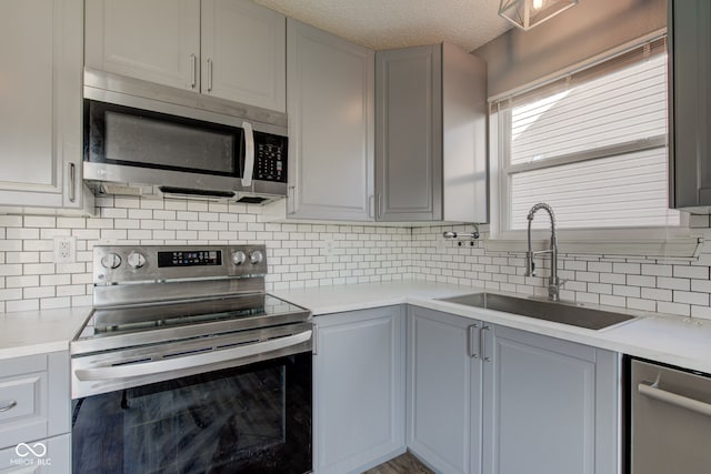 kitchen featuring gray cabinetry, a sink, backsplash, stainless steel appliances, and light countertops