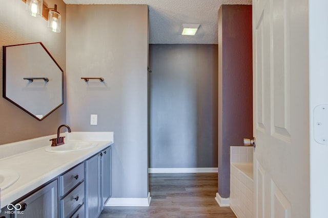 full bathroom with wood finished floors, baseboards, double vanity, a sink, and a textured ceiling