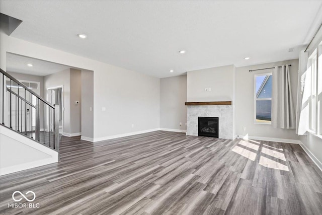 unfurnished living room with stairs, a tile fireplace, baseboards, and wood finished floors