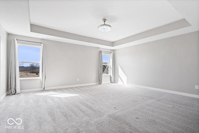 empty room featuring carpet flooring, a raised ceiling, and baseboards