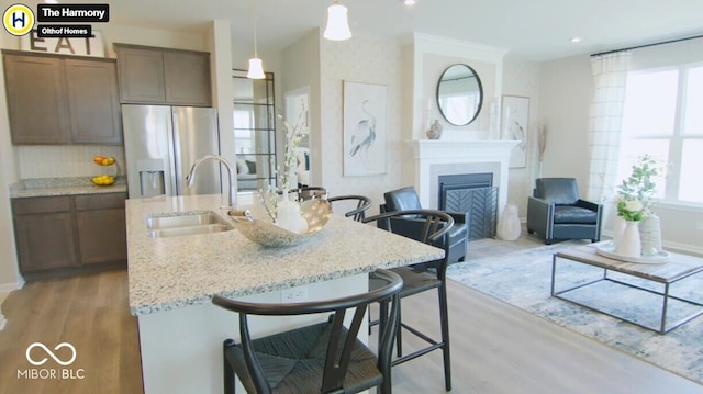 kitchen with a fireplace, stainless steel fridge with ice dispenser, hanging light fixtures, a sink, and a kitchen breakfast bar