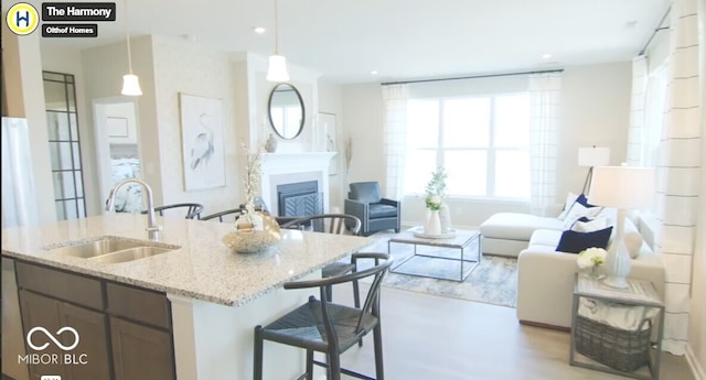 kitchen with light stone counters, a fireplace, a sink, open floor plan, and pendant lighting