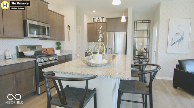 kitchen featuring wallpapered walls, a breakfast bar area, light stone counters, stainless steel appliances, and pendant lighting