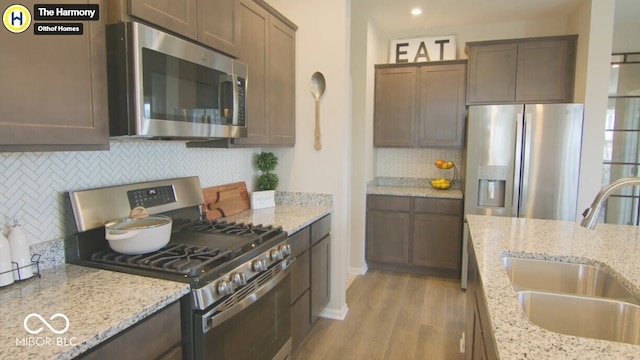 kitchen with stainless steel appliances, a sink, and light stone counters