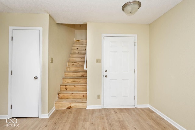 entryway featuring light wood-style floors, a textured ceiling, baseboards, and stairs