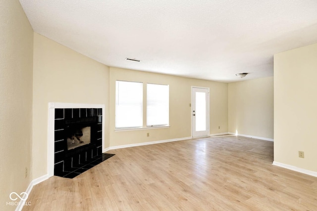 unfurnished living room featuring a tile fireplace, visible vents, baseboards, and wood finished floors