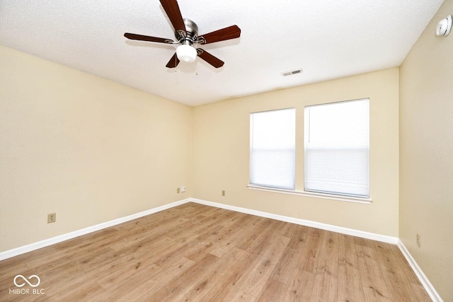 empty room featuring visible vents, light wood-style flooring, a ceiling fan, a textured ceiling, and baseboards