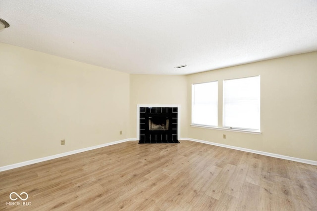 unfurnished living room with a textured ceiling, light wood finished floors, a fireplace, and baseboards