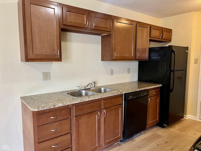 kitchen with a textured wall, light wood-style flooring, a textured ceiling, black appliances, and a sink