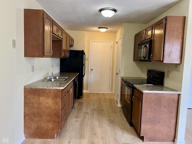 kitchen featuring light wood finished floors, baseboards, a textured ceiling, black appliances, and a sink