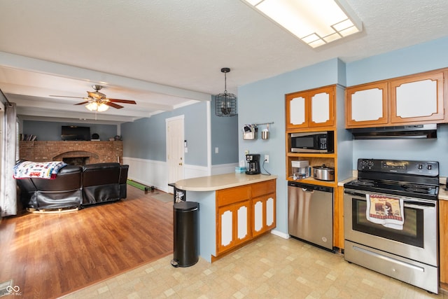 kitchen featuring light countertops, hanging light fixtures, appliances with stainless steel finishes, open floor plan, and under cabinet range hood