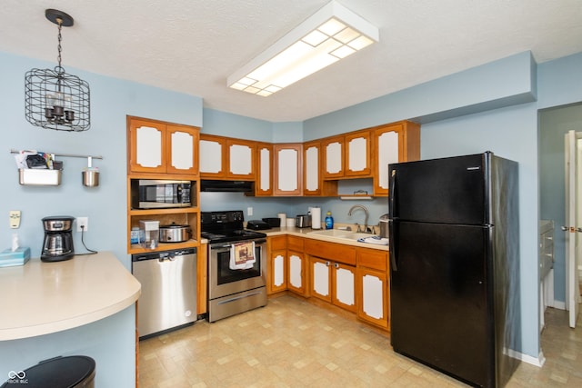 kitchen featuring appliances with stainless steel finishes, hanging light fixtures, light countertops, under cabinet range hood, and a sink