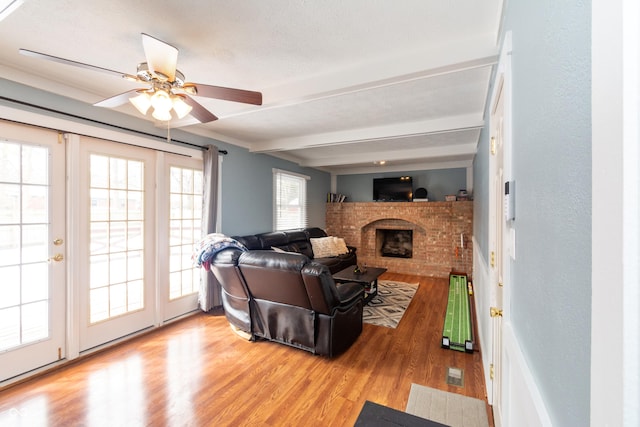 living area with beam ceiling, a fireplace, a textured ceiling, and wood finished floors