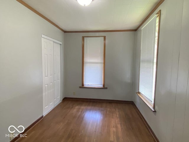 unfurnished bedroom featuring dark wood-style floors, a closet, ornamental molding, and baseboards