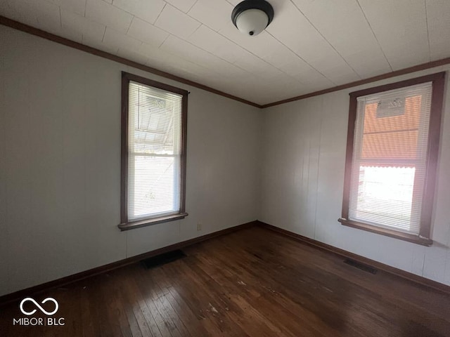 spare room with dark wood-style floors, baseboards, visible vents, and crown molding