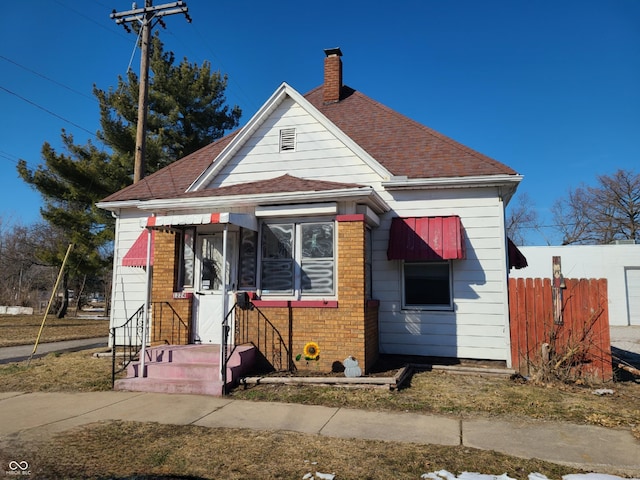 bungalow-style house with brick siding, a chimney, a shingled roof, and fence