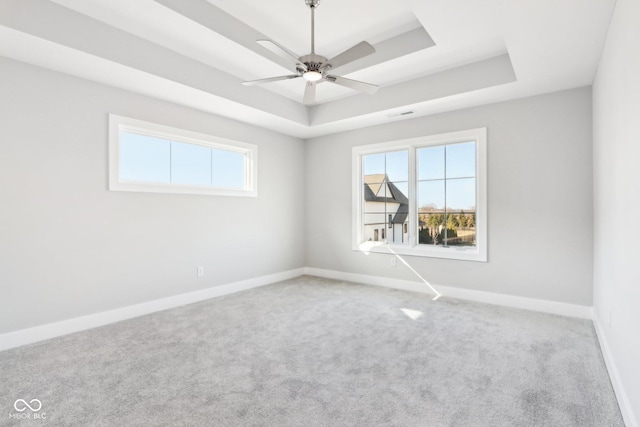 carpeted spare room with a raised ceiling, a ceiling fan, and baseboards