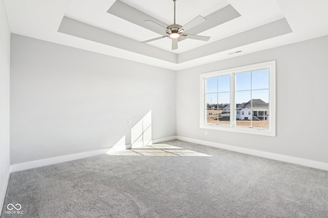 carpeted spare room with a raised ceiling, visible vents, ceiling fan, and baseboards