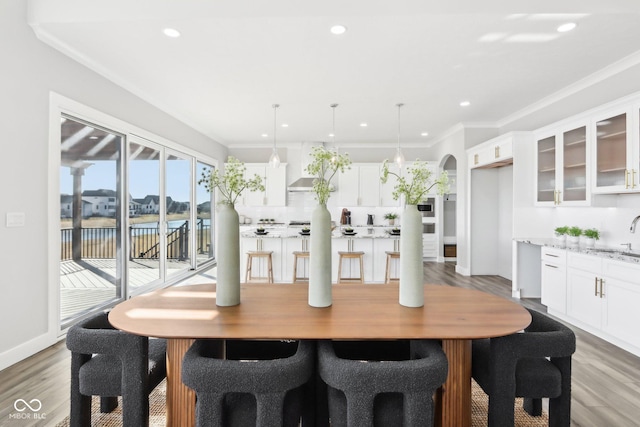 dining space featuring a water view, light wood finished floors, arched walkways, and ornamental molding