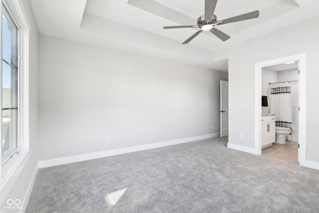 unfurnished bedroom with light carpet, a tray ceiling, multiple windows, and baseboards