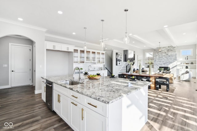 kitchen with glass insert cabinets, a kitchen island with sink, white cabinetry, pendant lighting, and a sink