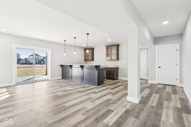 kitchen with light countertops, light wood-type flooring, glass insert cabinets, and pendant lighting