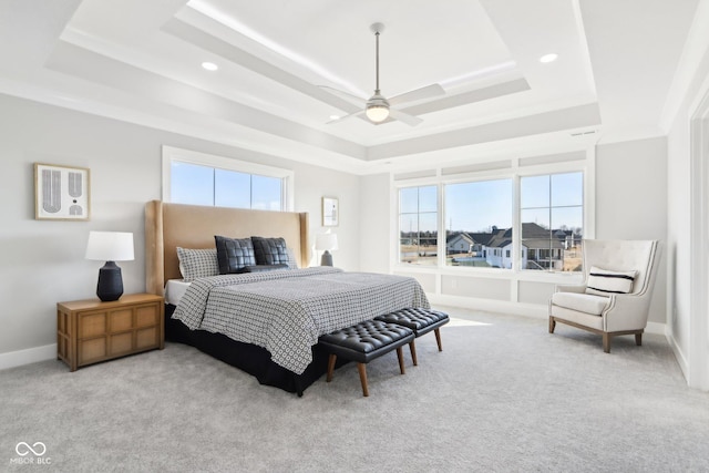 bedroom featuring light carpet, baseboards, a tray ceiling, and ceiling fan